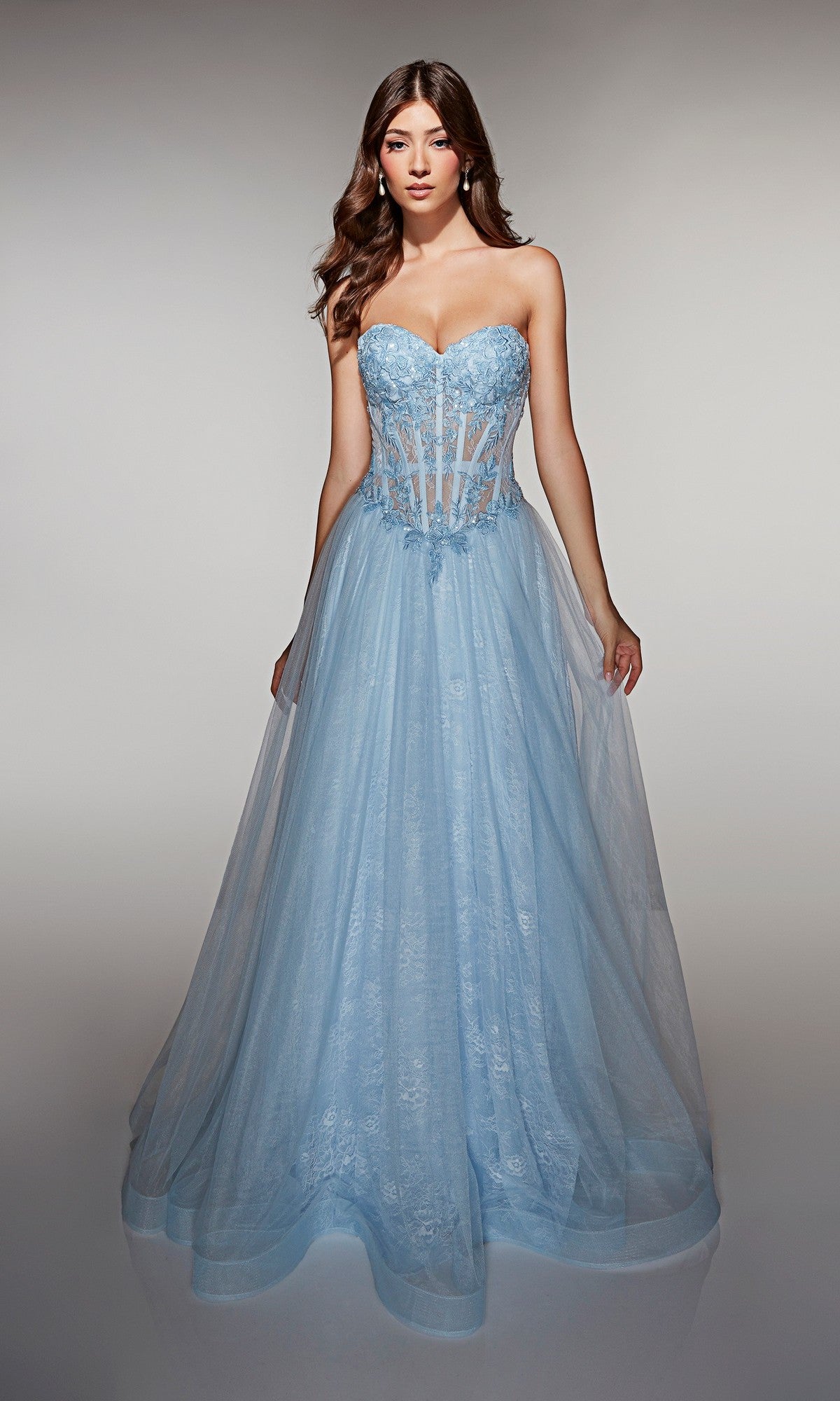 A woman in the Alyce 61984 long prom dress, a strapless light blue gown with a fitted corset bodice and a sweeping full tulle ball gown skirt.